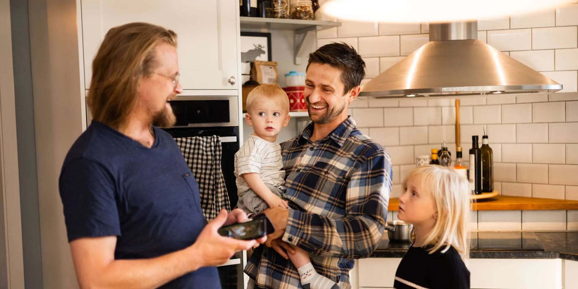 Två män och två barn i ett kök, som skrattar åt något i mobilen